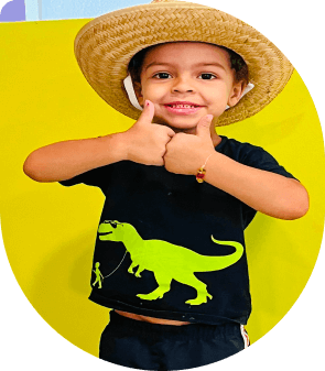 Smiling young boy in a preschool program in Las Vegas giving a thumbs up, wearing a cowboy hat and dinosaur shirt.