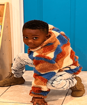 Preschool-aged child in Las Vegas wearing a colorful jacket, crouching playfully in a Pre-K learning center.